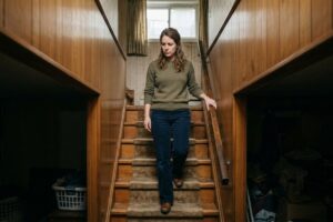 Femme hésitante dans l'escalier d'un sous-sol de maison ancienne, doute avant l'achat immobilier